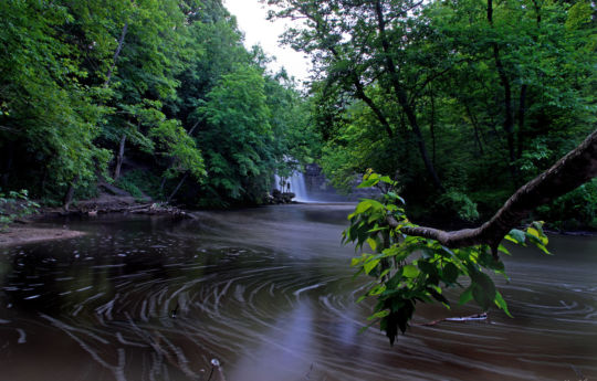 Man in the distance standing on rocks below Minneopa Falls in late spring | Minneopa State Park