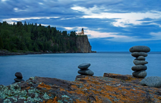 Rocks stacked on the beach with Split Rock Lighthouse in the background