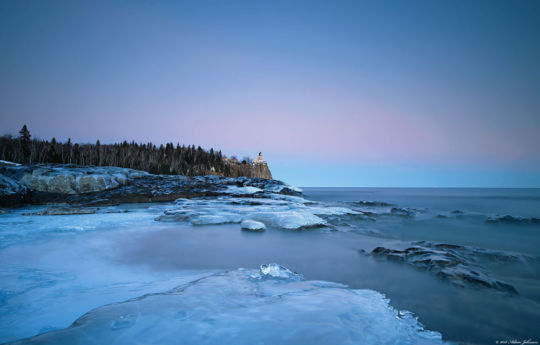 Waves rolling in on ice covered shoreline with Split Rock Lighthouse in the distance | Split Rock Lighthouse State Park