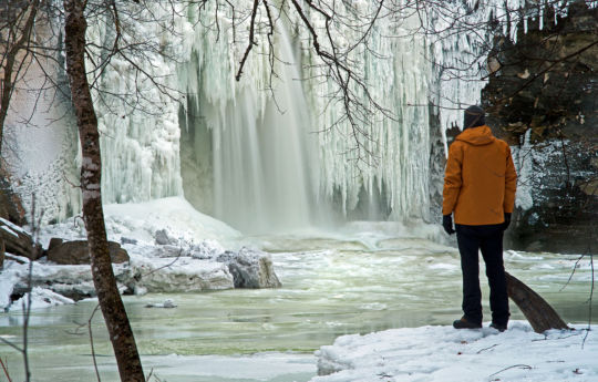 Man standing on the icy shore of Minneopa Creek and frozen Minneopa Falls | Minneopa State Park